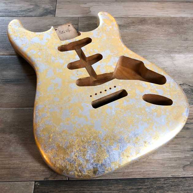 a Stratocaster-shaped guitar body covered in gold and silver leaf